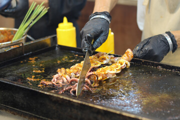 Chef hands grilling and slicing fresh spicy squid on a hot teppanyaki griddle.