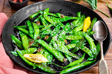 Asian food stir fried green peas with sesame seeds in a pan close up