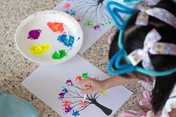 Group of children dipping cotton buds in paint and stamping colorful leaves on tree drawing, exploring creativity, imagination, and hands-on learning in early education.