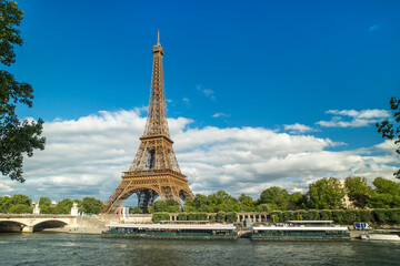 Fototapeta premium Eiffel Tower in Paris with Seine River and blue sky, symbolizing romance, architecture, travel, tourism, European landmark, and cultural heritage under scenic urban atmosphere.