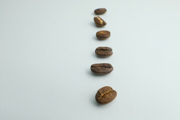 Close up of roasted coffee beans arranged in a vertical line on white background. Minimal concept for coffee culture, cafe branding, food industry, and creative advertising design.
