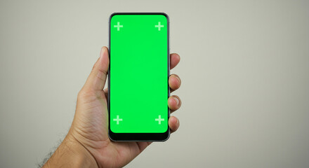 Hand holding modern smartphone with vibrant green screen and tracking markers, ready for creative content
