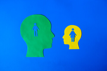 Two head silhouettes (green and yellow) with gender figure cutouts inside, on a blue background.