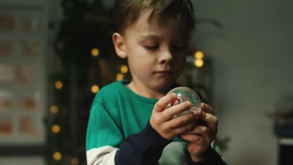 Child shaking Christmas snow globe in his hands. Christmas and New Year celebration.