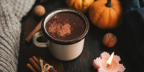 Cozy autumn scene with mug of hot chocolate, pumpkins, spices and candles on rustic dark wooden background, warm seasonal atmosphere