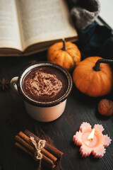 Cozy autumn scene with mug of hot chocolate, book, pumpkins, spices and candles on rustic dark wooden background, warm seasonal atmosphere