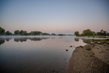 Morgendlicher Nebel über einem ruhigen Fluss mit sanften Uferbäumen