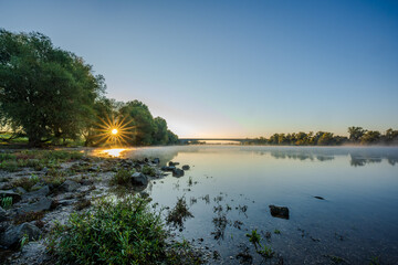 Sonnenaufgang über dem ruhigen Fluss mit Nebel und buntem Himmel am frühen Morgen
