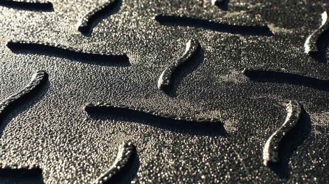 Industrial metal surface with raised tread texture illuminated by sunlight, showing material design, traction pattern and durability used in machinery flooring, engineering and manufacturing systems