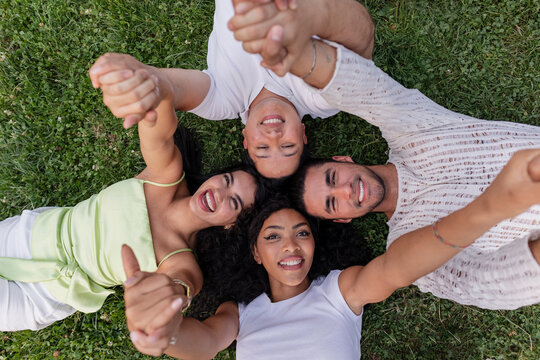 Diverse friends lying on grass holding hands together