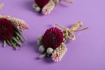 Stylish boutonnieres with flowers on purple background, closeup