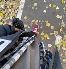 Person strolls on a path lined with colorful autumn leaves, capturing the moment with a camera