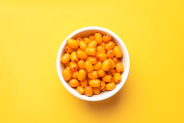 Ripe sea buckthorn berries in bowl on yellow background, top view
