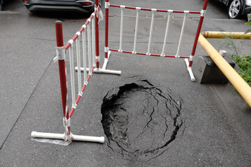 A large hole in the road with a red and white barrier in front of it