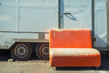 Old shabby orange sofa stands near trailer on street