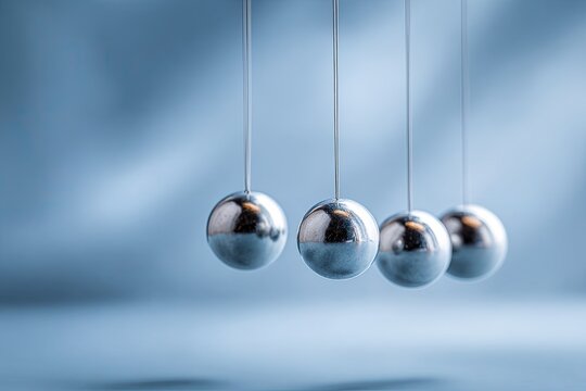 A close-up of Newton's cradle, showcasing reflective metal spheres suspended by thin cords - Powered by Adobe