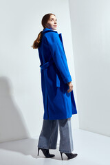a beautiful woman in a long blue coat on a light background