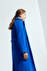 a beautiful woman in a long blue coat on a light background