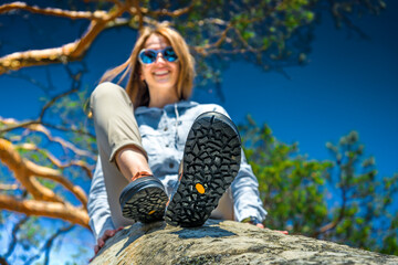 Smiling woman on rock, hiking boots sole in focus, mountain adventure and outdoor lifestyle