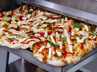 Freshly baked pizza with tomato sauce and mozzarella cheese, topped with basil, ready to serve in a busy kitchen
