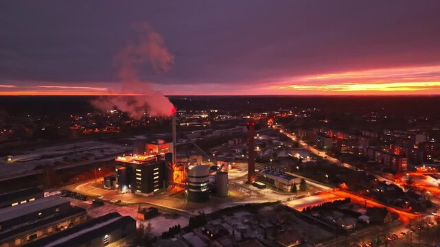 Evening aerial of energy facility at sunset with glowing smoke stack and lights