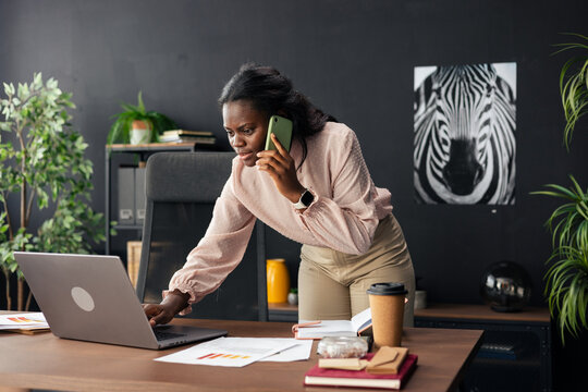 African american businesswoman multitasking, working on laptop and talking on phone