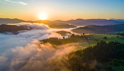 Fototapeta premium An aerial view showcases a stunning sunrise above rolling hills, with morning fog creating a soft layer over the green landscapes