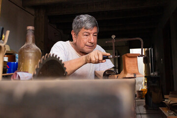An elderly Colombian luthier with a hacksaw in his hand polishing a guitar inside a workshop in Neiva, Huila, Colombia. Concept of handmade