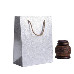 Shiny, patterned gift bag with rope handles, next to a wooden urn on a black background