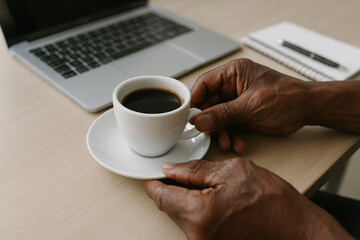 Hands of african american man holding coffee cup at cafe table with laptop and notepad. concept of relaxation, modern workspace, coffee break