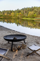 Tranquil Outdoor Setting Featuring a Fire Pit by the Water's Edge Surrounded by Lush Greenery and Reflective Calm Water in a Peaceful Natural Environment