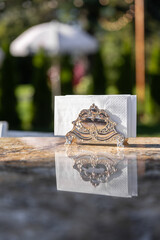 Elegant Silver Napkin Holder with a White Napkin Reflected on a Polished Surface in a Beautiful Outdoor Setting Surrounded by Lush Greenery and Soft Lighting.