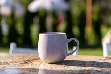 A Beautifully Crafted Lavender Mug on an Outdoor Table Surrounded by Greenery and Sunlight, Perfect for Enjoying a Warm Beverage During a Relaxing Day