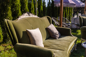 Cozy and Elegant Green Sofa Decorated with Soft Pillows Surrounded by Lush Foliage and Outdoor Furniture in a Beautiful Garden Setting