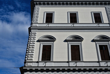 white stucco elevation of residential building in Rome, Italy. vertical wood windows with stone trims and arches. classic design. staggered stone corner. blue sky background. travel, tourism concept
