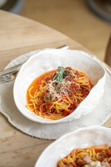 Spaghetti with meatballs served in a white plate, topped with tomato sauce, grated cheese, and fresh herbs
