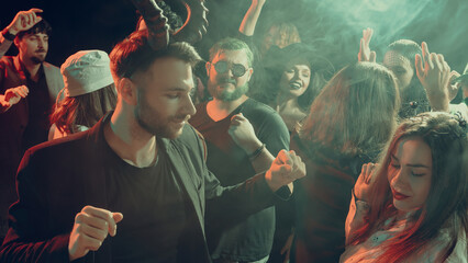 Excited young people in themed costumes dancing under neon smoke lights. Concept of entertainment, holiday advertising, student life, youth energy and music culture branding.