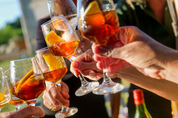 Friends drinking outside in summer sun, toasting with orange wine, martini, vermouth at beach bar cafe