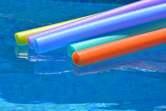 Colourful pool noodles floating on water in swimming pool