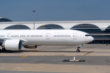 A large commercial aircraft is parked at an airport, showcasing its sleek design against a backdrop of a modern terminal with curved roofs and bright daylight
