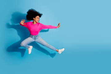Obraz premium Young woman in pink jumper and casual jeans jumping joyfully against a vibrant blue background expressing happiness