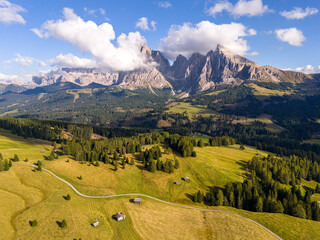 Aerial view over meadows in front of Alpe di Siusi peaks, in Dolomites, Italy. Beautiful hut on alpine plateau Seiser Alm. Wooden cabins in south Tyrol. Dolomites UNESCO World Heritage.