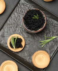 Black caviar in a round tartlet and a black bowl, a delicious appetizer