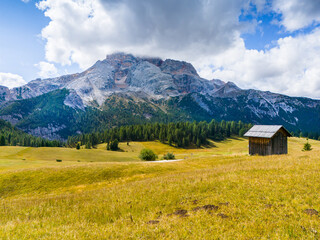 Beautiful landscape in Dolomites, Italy.  Malga Prato Piazza meadow and big mountain summit and ridge. South Tyrol region in Italy. Trekking and bike road in Italy Dolomites. Wooden cabin hut.