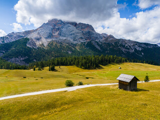 Beautiful landscape in Dolomites, Italy.  Malga Prato Piazza meadow and big mountain summit and ridge. South Tyrol region in Italy. Trekking and bike road in Italy Dolomites. Wooden cabin hut.