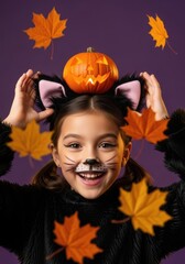 Happy asian girl in cat costume holding pumpkin above head. Happy Halloween.  Purple background, autumn leaves falling. 