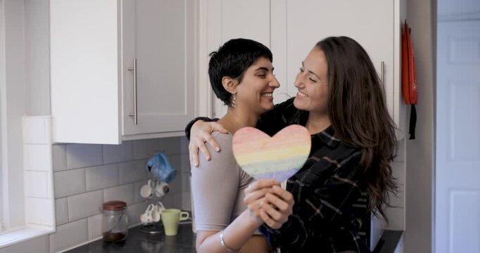 Happy girl friends lesbian couple embracing and holding a heart shaped rainbo