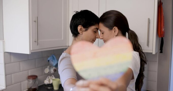 Happy girl friends lesbian couple embracing and holding a heart shaped rainbo