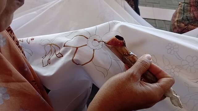 hand holding a canting to batik cloth
