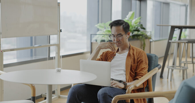 Senior Asian businessman wearing headset celebrates success during online meeting in modern co-working space. Remote work and business communication concept	